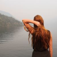 woman standing looking at lake in misty weather with hand in hair