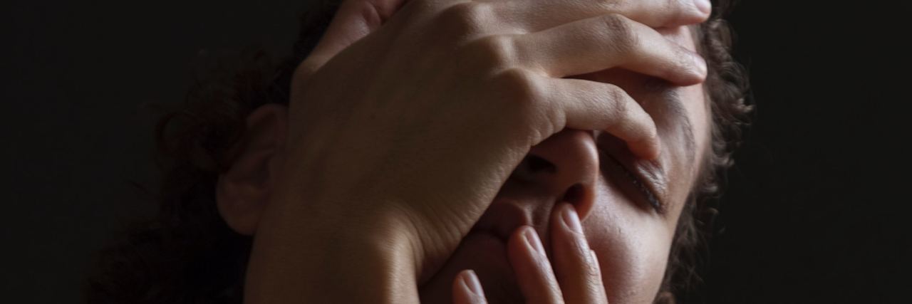 What I Mean When I Say I Am Sick of Anxiety woman in mostly darkness with hands covering face in upset