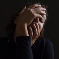 woman in mostly darkness with hands covering face in upset