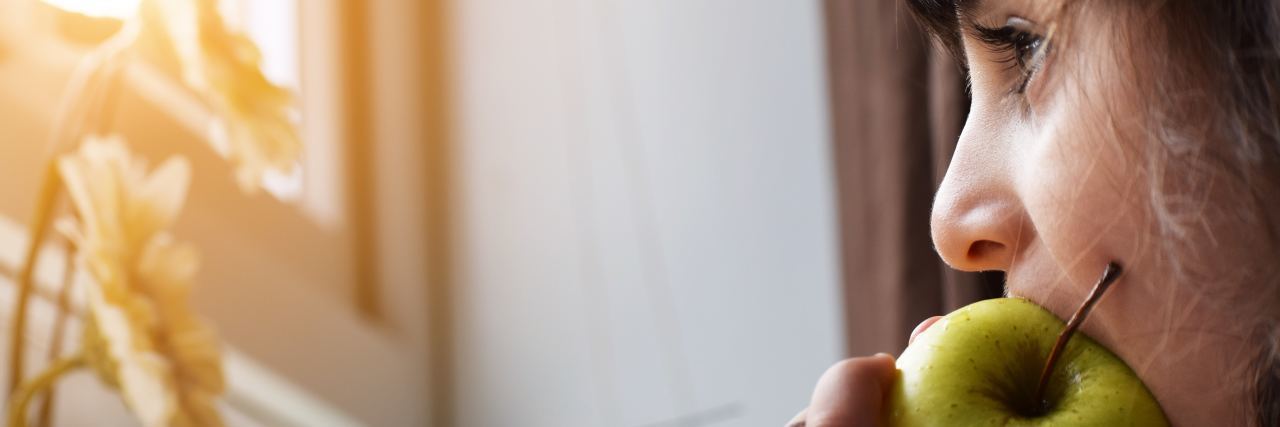 close up of woman looking out of window eating an apple