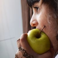 close up of woman looking out of window eating an apple