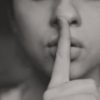 black and white photo of woman with finger to lips in hush motion