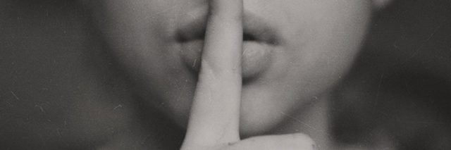 black and white photo of woman with finger to lips in hush motion