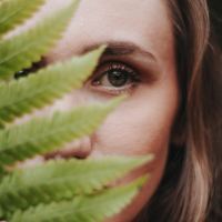 woman looking into camera and covering face with fern leaves