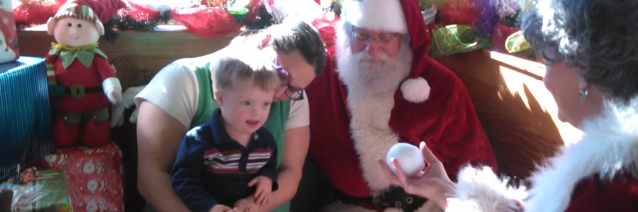 Little boy with Down syndrome sitting on his aunt's lap while visiting Mr. and Mrs. Claus