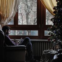 man reading book by window at Christmas with tree beside him