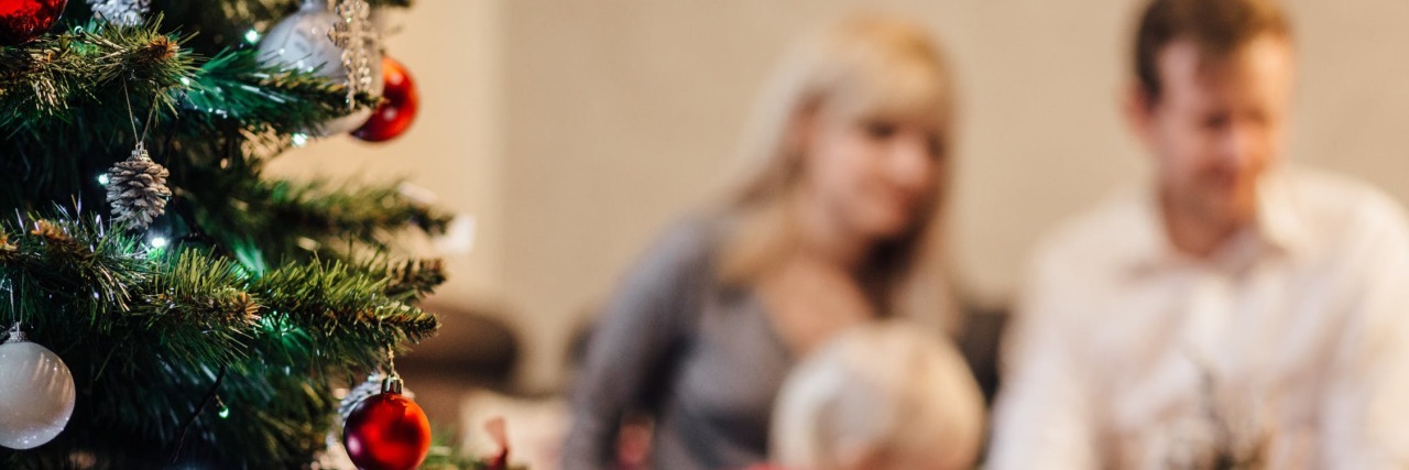 How to Survive Holiday Gatherings With Chronic Illness, Anxiety man and woman sitting at a table with their young child by a christmas tree