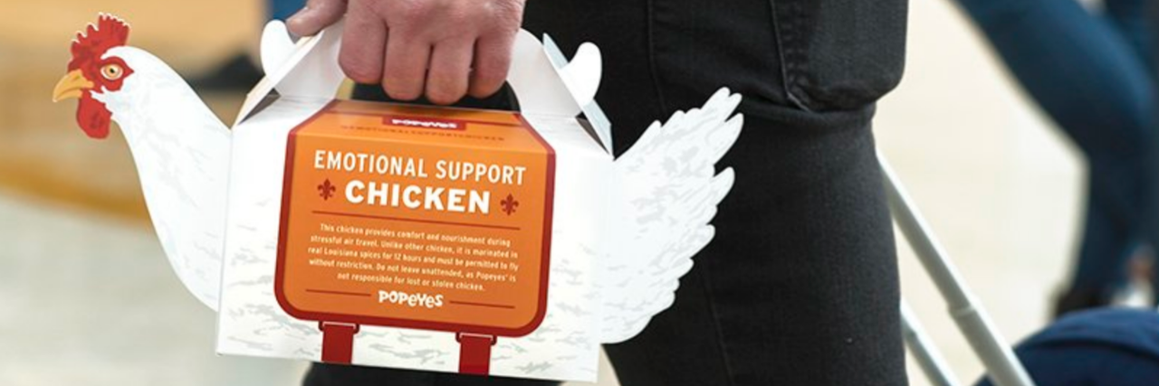 Popeyes to Offer 'Emotional Support Chickens' in Philadelphia Airport Popeyes chicken-shaped box with a man holding the handles at the top of the chicken.