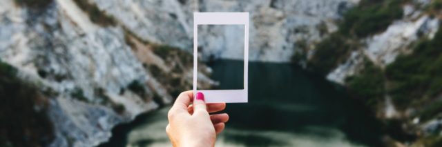 close up of person's hand holding empty polaroid photo frame against mountain and lake environment