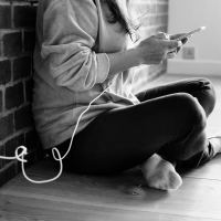 black and white photo of woman sitting on floor with phone plugged into power socket