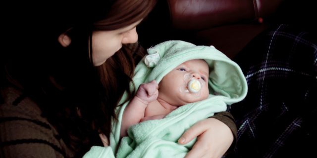 mother holding baby wrapped in towel with unknown expression
