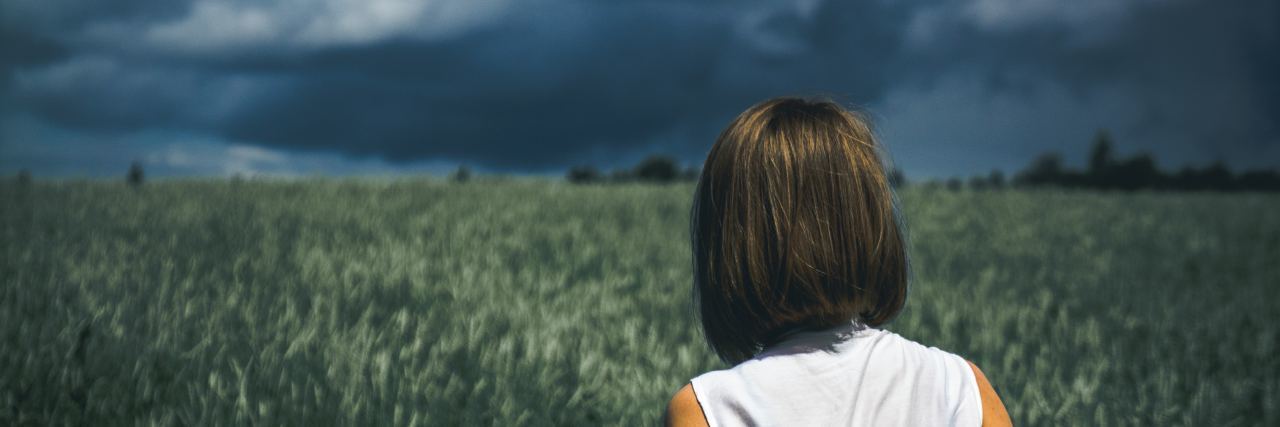 woman standing in field looking at distant storm clouds