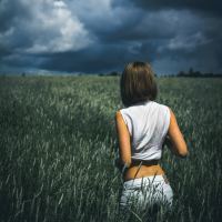 woman standing in field looking at distant storm clouds
