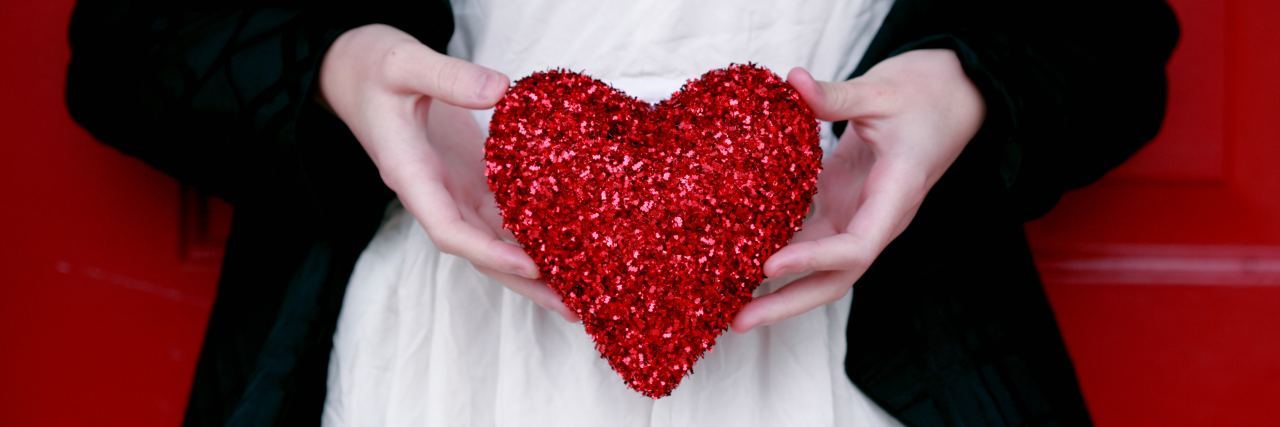 close up of woman holding glitter red heart against white dress