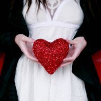 close up of woman holding glitter red heart against white dress