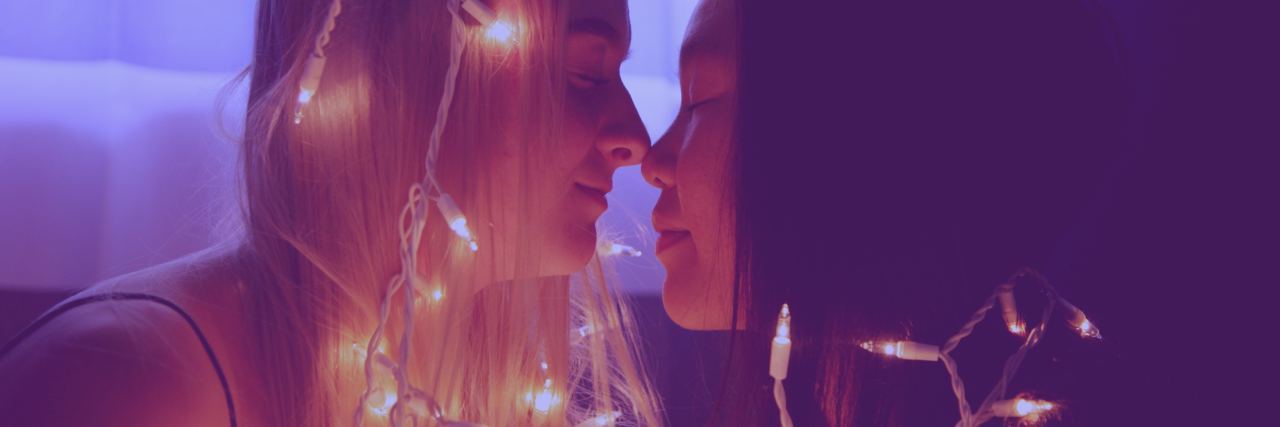 What to Know About Anxiety and Relationships young female same-sex couple touching noses and wrapped in fairy lights