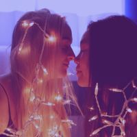young female same-sex couple touching noses and wrapped in fairy lights