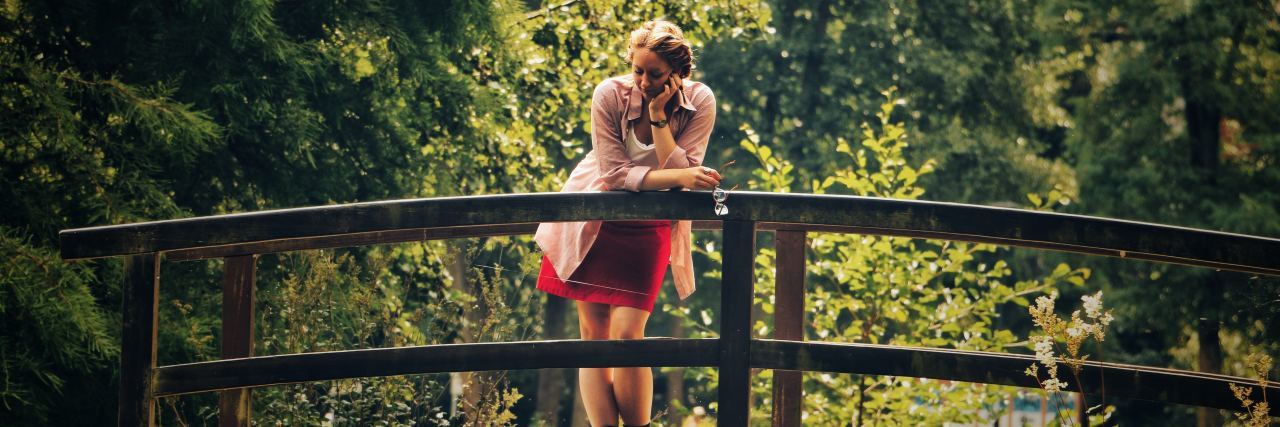 What to Do When Anxiety Makes You Think Everyone Hates You young woman standing on bridge in forest leaning head on hand