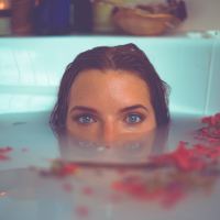 woman partially submerged in bath with flowers looking into camera