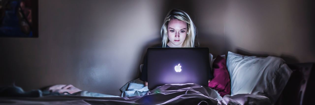 young woman sitting upright in bed late at night with laptop open in front of her
