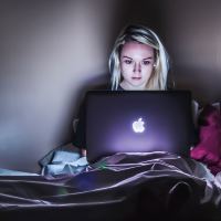 young woman sitting upright in bed late at night with laptop open in front of her