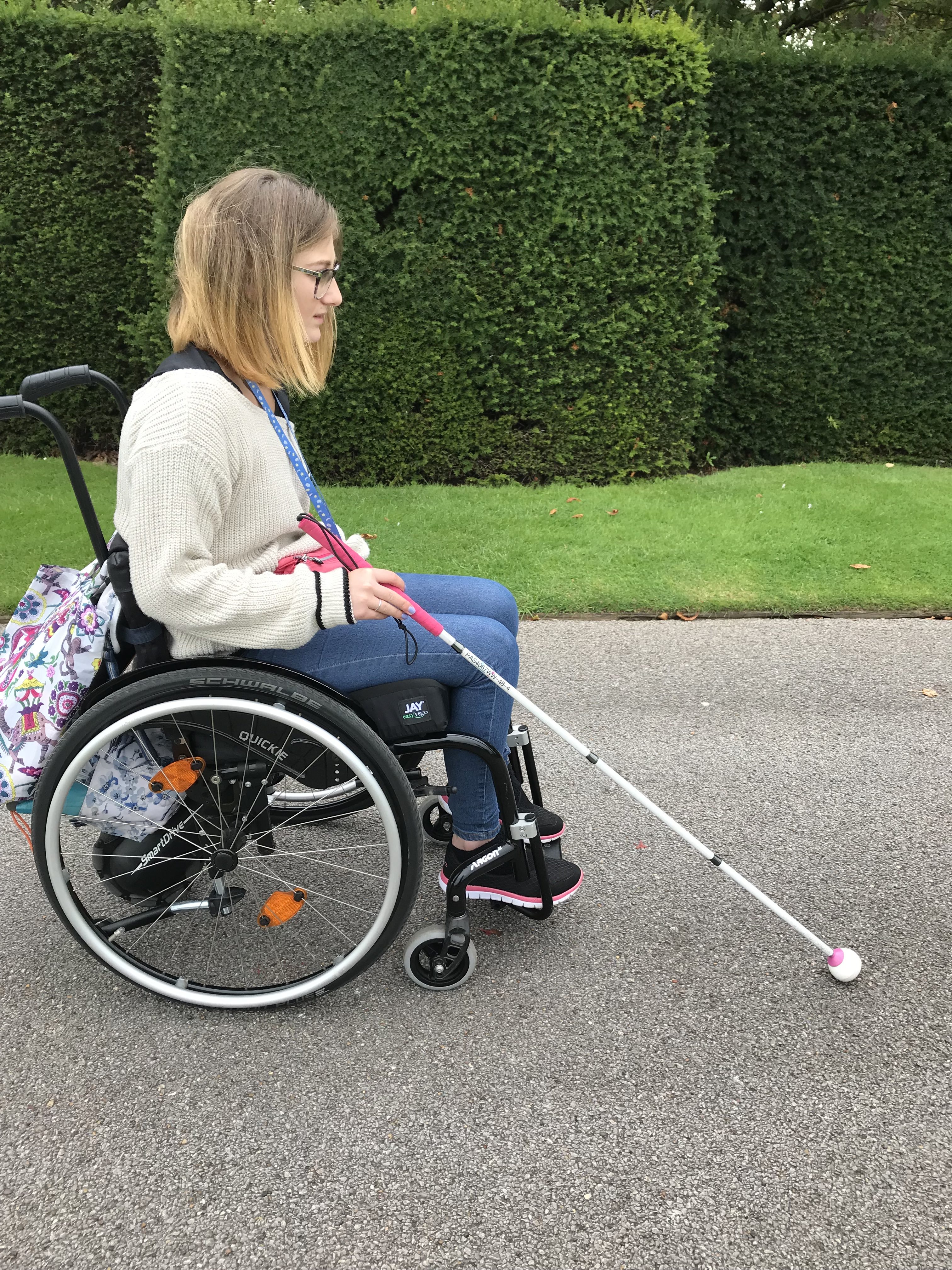 Leah using her white cane and wheelchair outdoors.