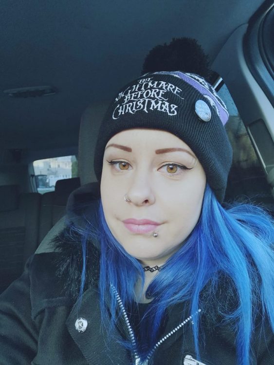 woman with long blue hair sitting in her car wearing a jacket and beanie