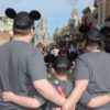 dad, mom and son with arms around each other wearing mickey ears, facing disneyland