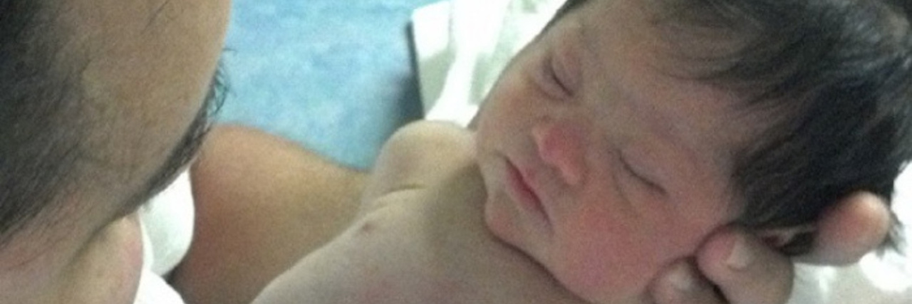 I Learned About Down Syndrome From My Daughter Baby with Down syndrome sleeping while her dad holds her.