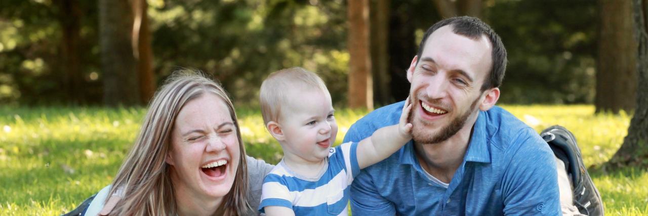 A Letter to Myself as I Parent a Child With a Disability Family lying on a picnic blanket outside, mom and dad laughing with their son sitting between them touching his dad's face.