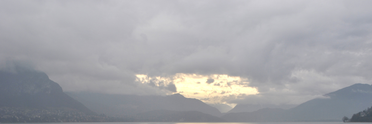 girl with umbrella facing a lake and clouds in the sky