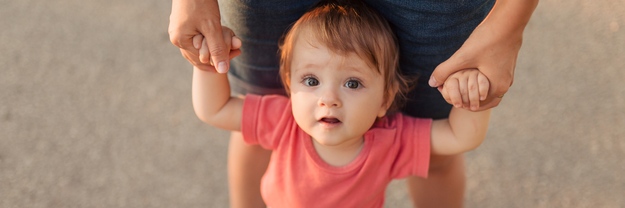 Mother holding hands of child who is looking up with curiosity.