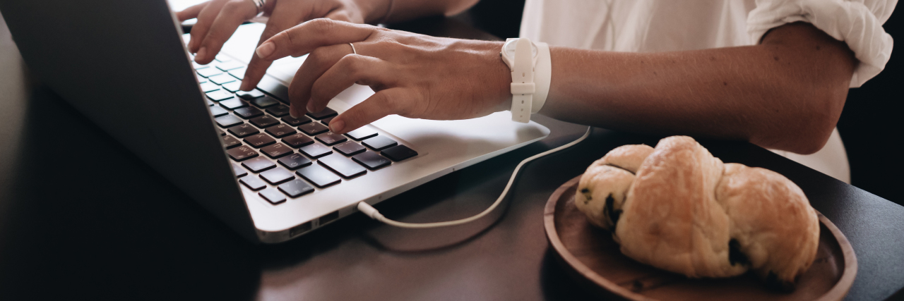 close up of young woman working on laptop with pastry on plate beside her