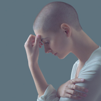 photo of woman with shaved head looking sad or thoughtful with hand to brow