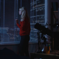 Medium wide shot of a lonely woman looking out a window at night then walking away