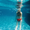 A woman in a red bikini floating underwater in a pool