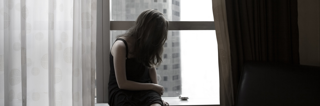How Weight Shaming Harms Women With Chronic Illnesses Sad woman sits in a window.