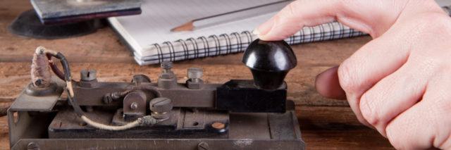 Hand tapping morse code on an antique telegraph machine.