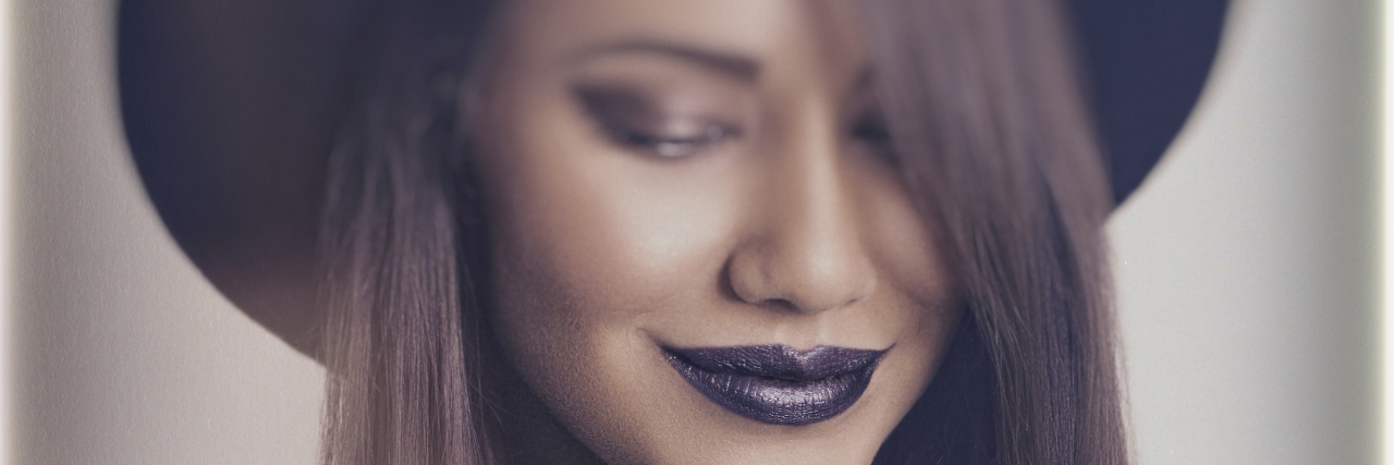 Living With Juvenile Idiopathic Arthritis Young woman wearing black lipstick and hat.