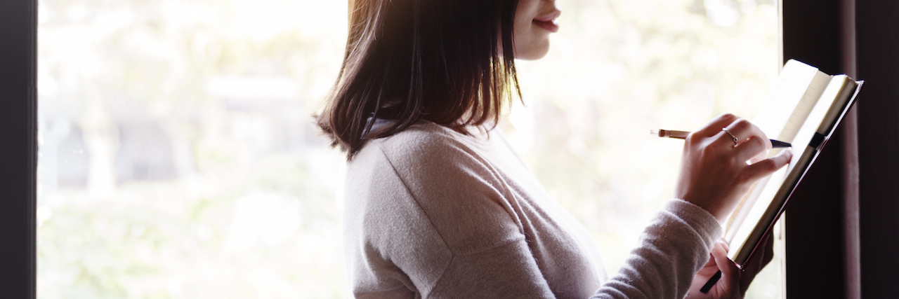 Why Gratitude Lists Make Me Feel Guilty - and What I Do Instead A woman standing up, writing in a notebook