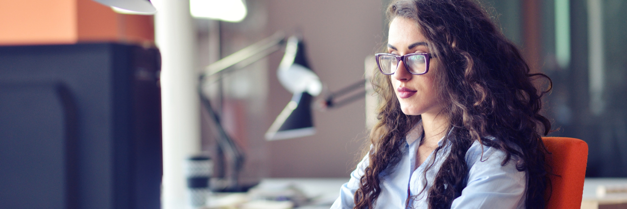 Why Being At Work Doesn't Mean I'm Not Sick Anymore Portrait of smiling pretty young business woman in glasses sitting on workplace.