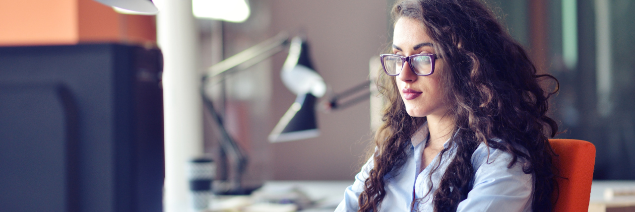 Portrait of smiling pretty young business woman in glasses sitting on workplace.
