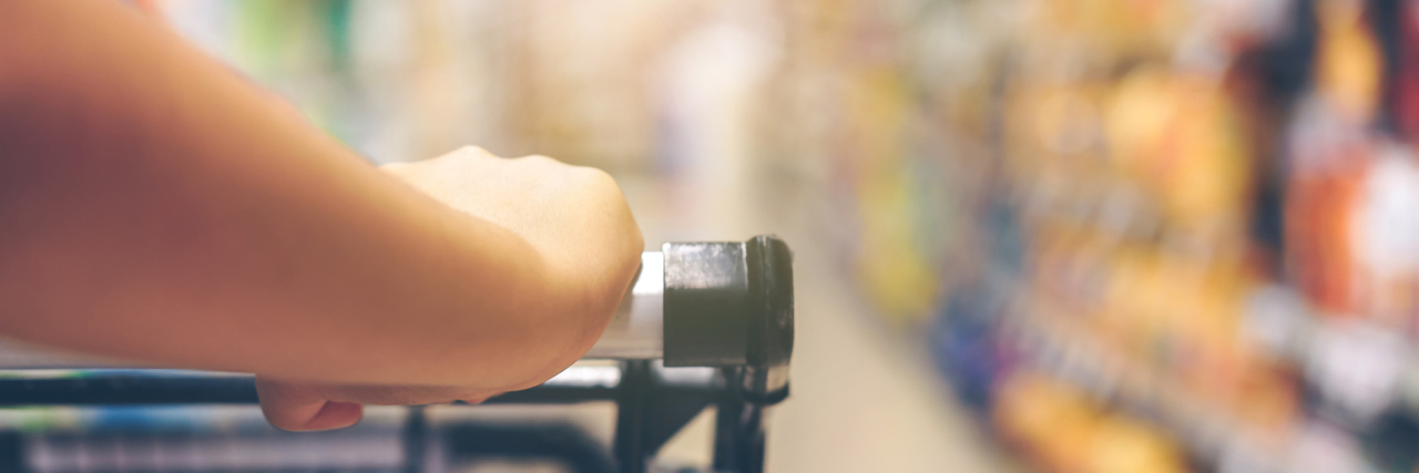 When You Have a Panic Attack While Grocery Shopping woman's hand on supermarket trolley or shopping cart with blurred background of aisle