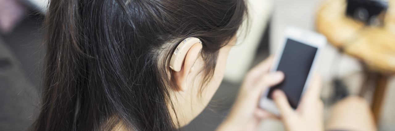 Young woman with hearing aid using mobile phone.