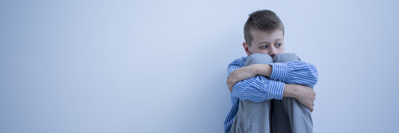 Struggling to Take My Son to See a Therapist Boy sitting on floor hugging his knees.