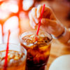 close up of two glasses of soda with straws and woman's hand