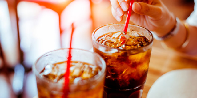 close up of two glasses of soda with straws and woman's hand