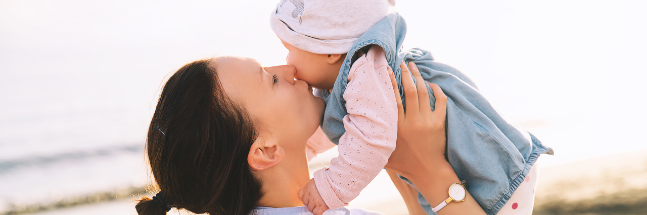 Parenting a Daughter With a Congenital Heart Defect a mom is holding her baby and kissing her on the cheek at the beach