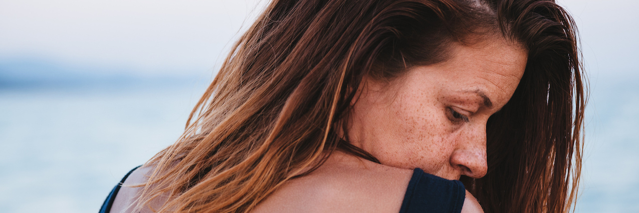 A woman at the beach, with her head rested at her shoulder, a sad expression on her face