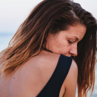 A woman at the beach, with her head rested at her shoulder, a sad expression on her face
